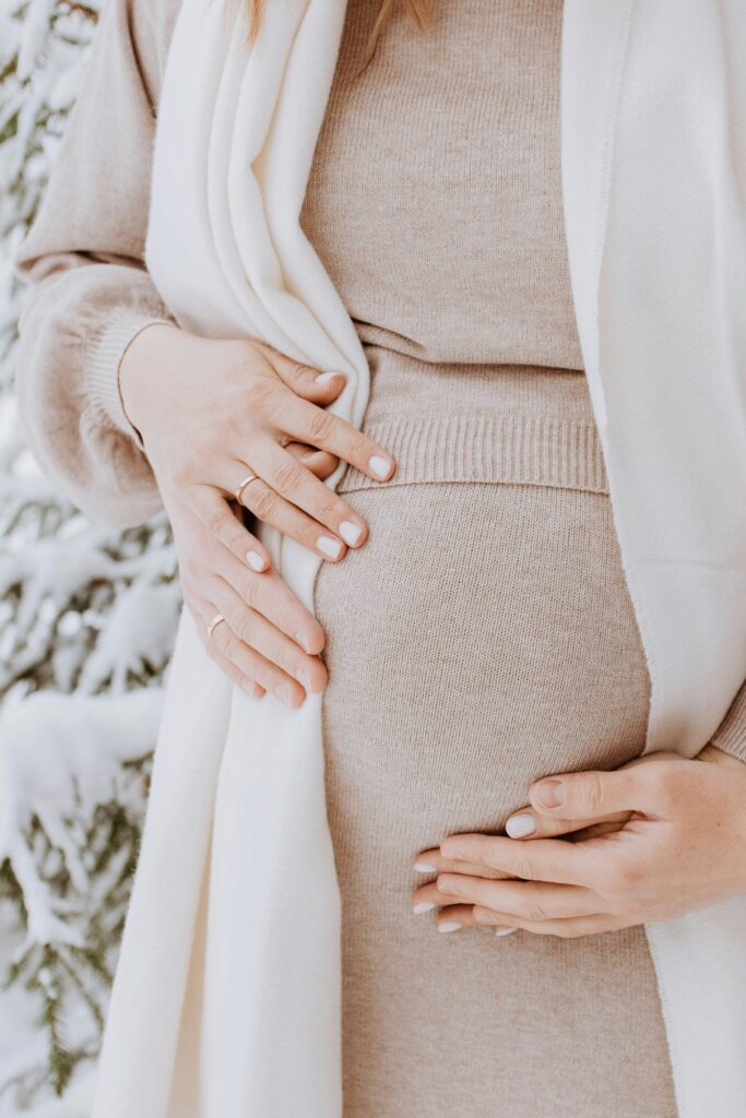 Mãos sobre a barriga de uma grávida, envolta num xaile branco, num dia de neve